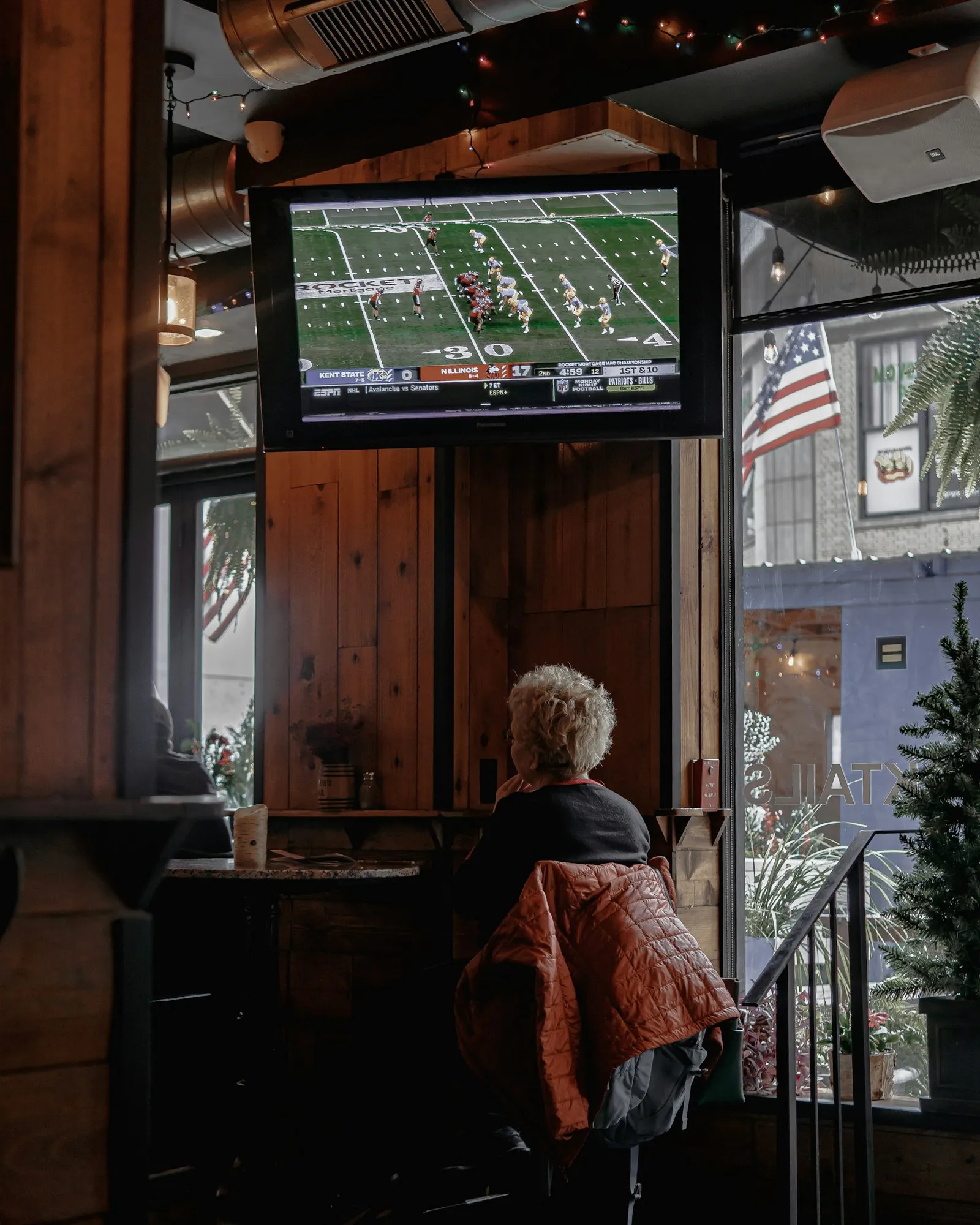 A large screen playing content above the counter in a warm, wood-paneled bar